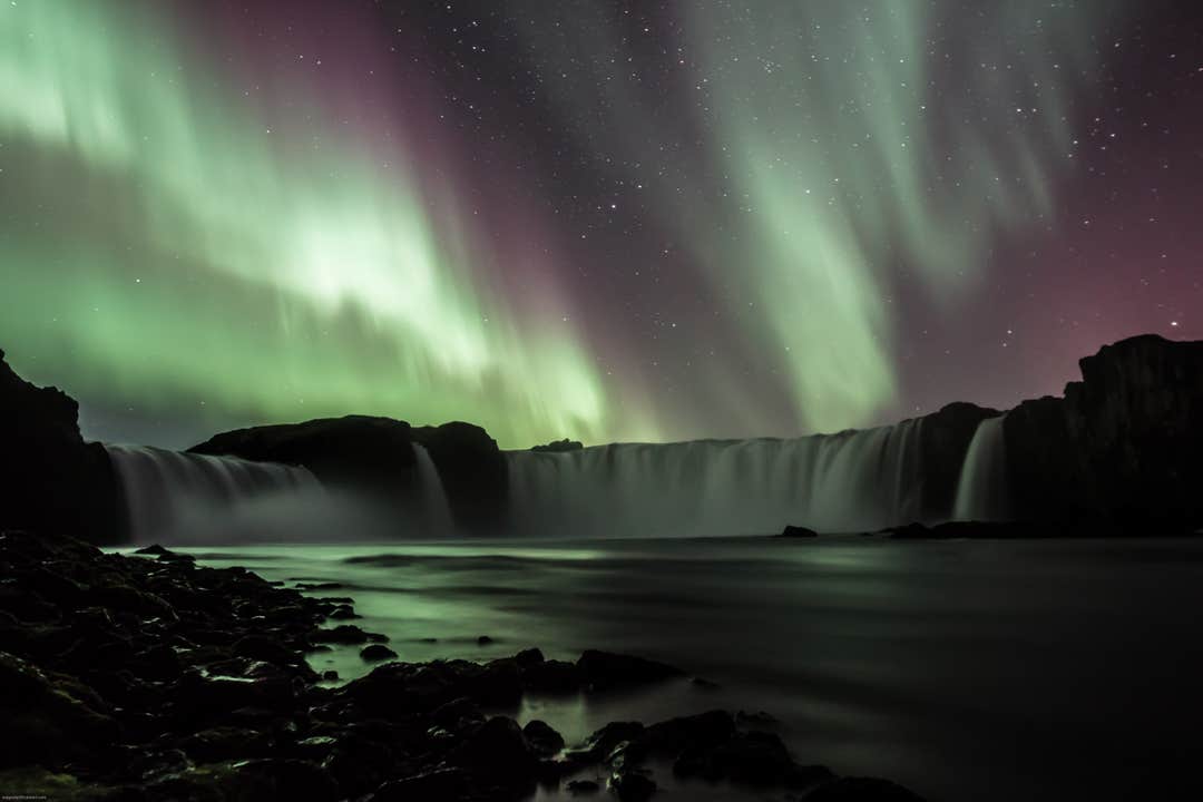 Nordlyset strækker sig hen over himlen over vandfaldet Godafoss i Nordisland.