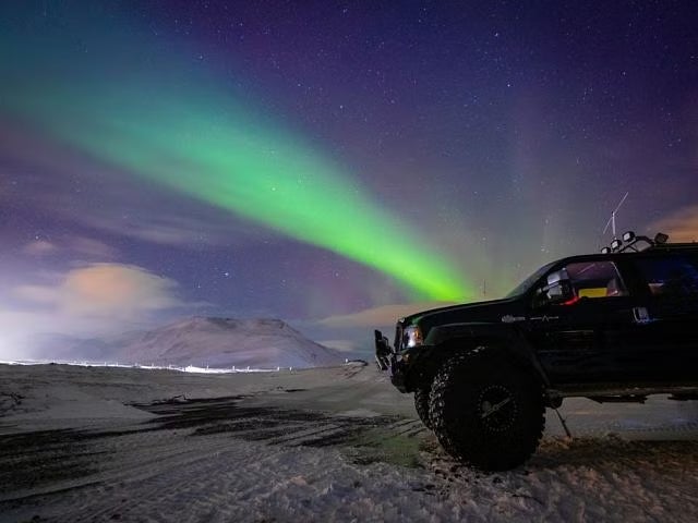 A super jeep parked in a snowy landscape with the northern lights glowing in the skies.