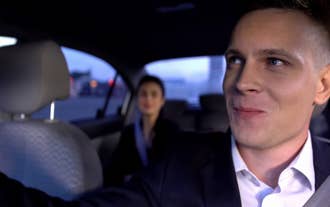 Een privéchauffeur glimlacht naar de reiziger op de achterbank.