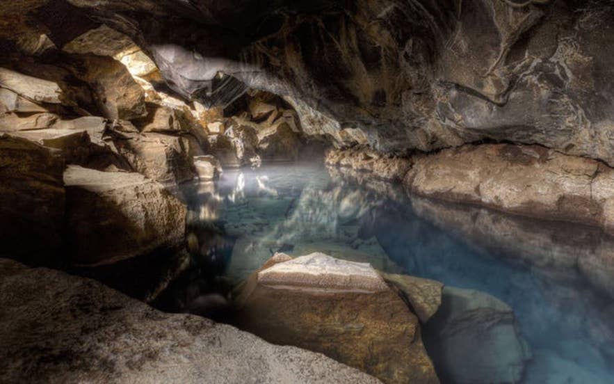 Sunlight streams through an opening onto the blue geothermal spring inside Grjotagja Cave.