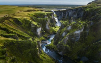 Luchtfoto van Fjadrargljufur Canyon in IJsland, met steile, met mos bedekte kliffen en een kronkelende rivier die het landschap doorsnijdt.