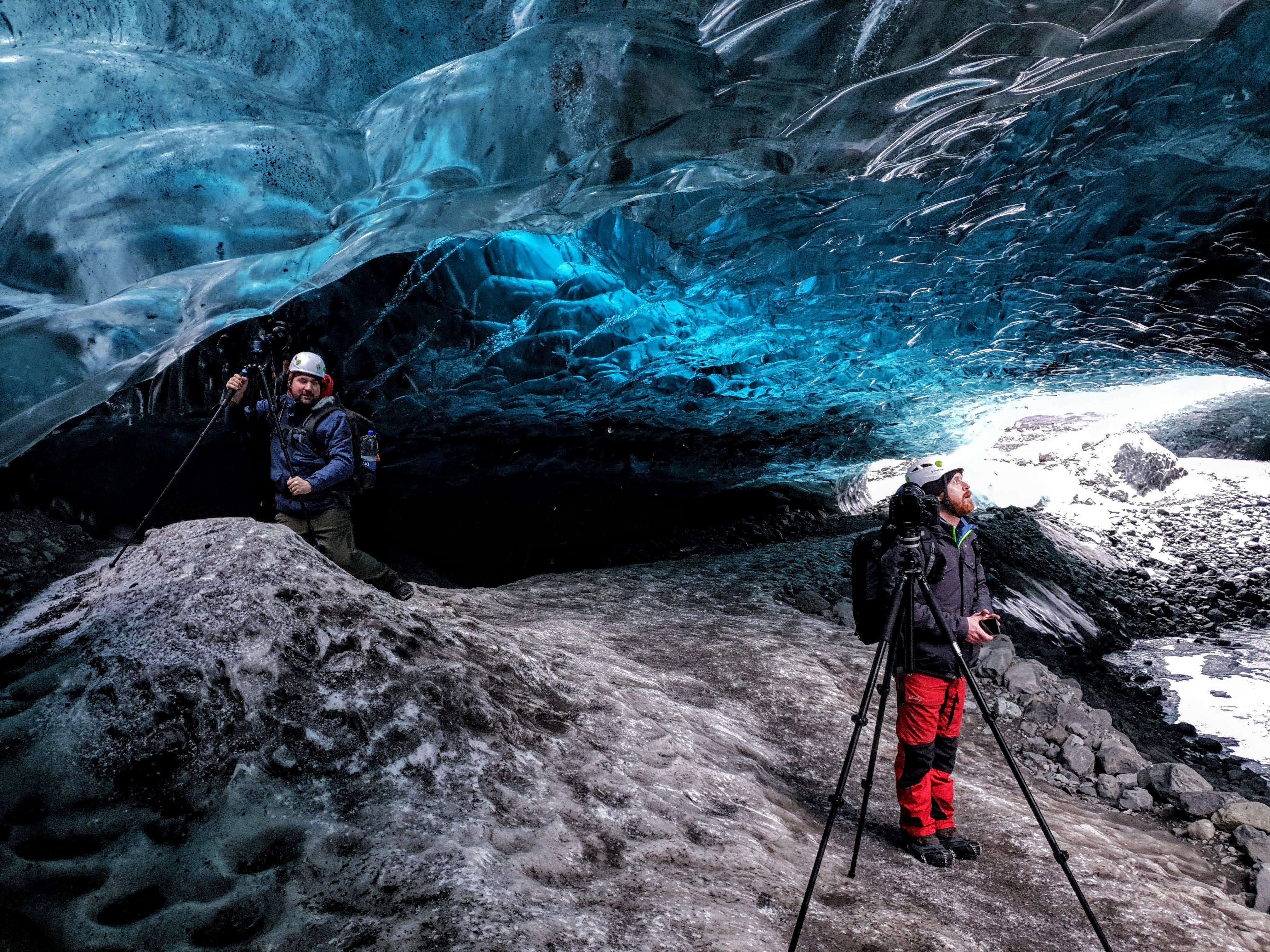 A photographer stands beside a tripod in a blue ice cave in Iceland.