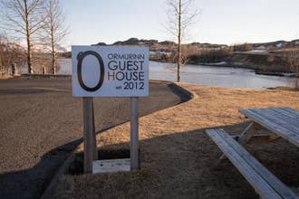 Sign for Ormurinn Guesthouse est. 2012 by a river with scenic East Iceland landscape