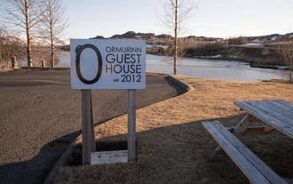Sign for Ormurinn Guesthouse est. 2012 by a river with scenic East Iceland landscape