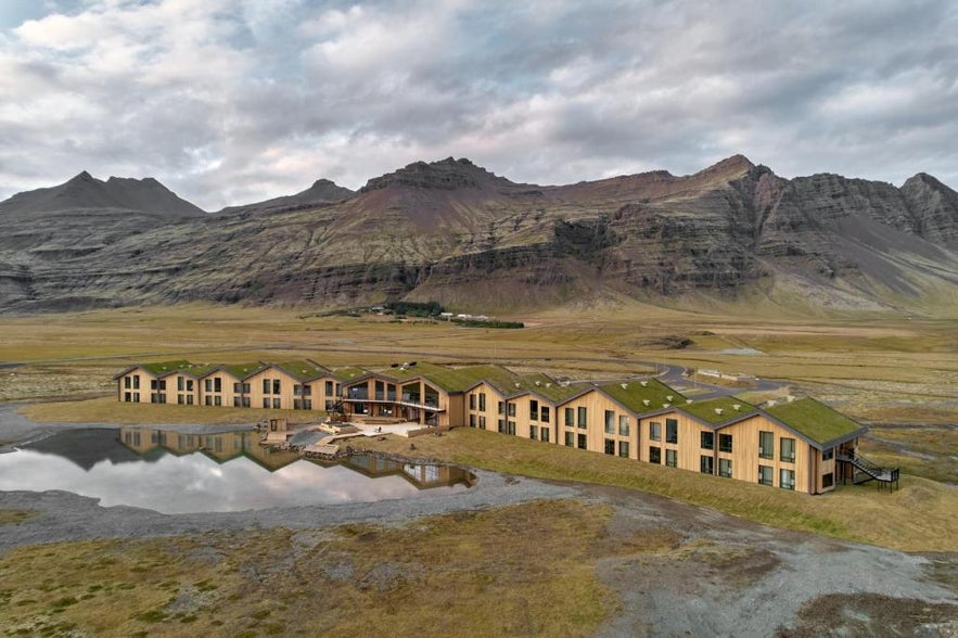 Modern Glacier Lagoon Hotel with grass-covered roofs near Jokulsarlon Glacier Lagoon in Iceland, set against dramatic mountain scenery and surrounded by open plains and reflective water.