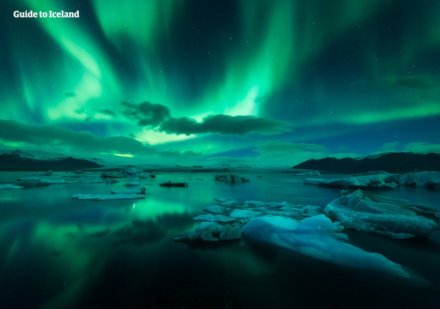 Vibrantes auroras boreales verdes sobre icebergs flotantes en la Laguna Glaciar de J&ouml;kuls&aacute;rl&oacute;n en Islandia, con la aurora reflejada en el agua helada bajo un cielo despejado.