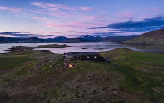 A zoomed out photo of Hvammsvik Hot Springs facilities with the ocean and mountains in the background.