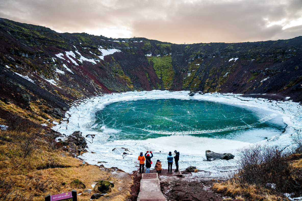 A group of travelers enjoying the views of Kerid crater's frozen lake during winter in Iceland.