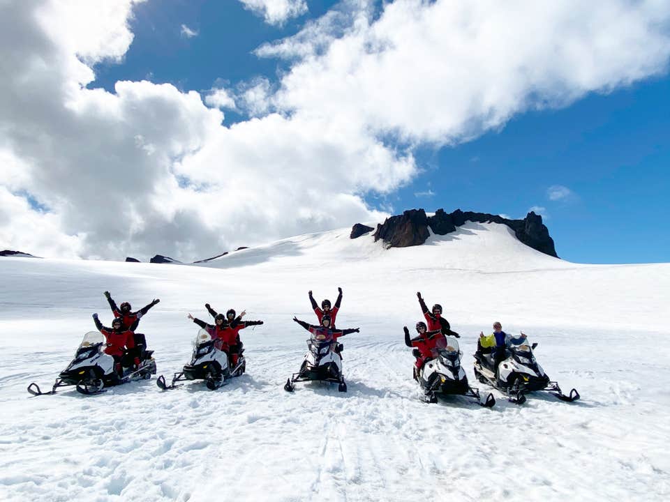 ヴァトナヨークトル氷河(Vatnajokull)の上でスノーモービルに乗り、両手を上げている人々のグループ。