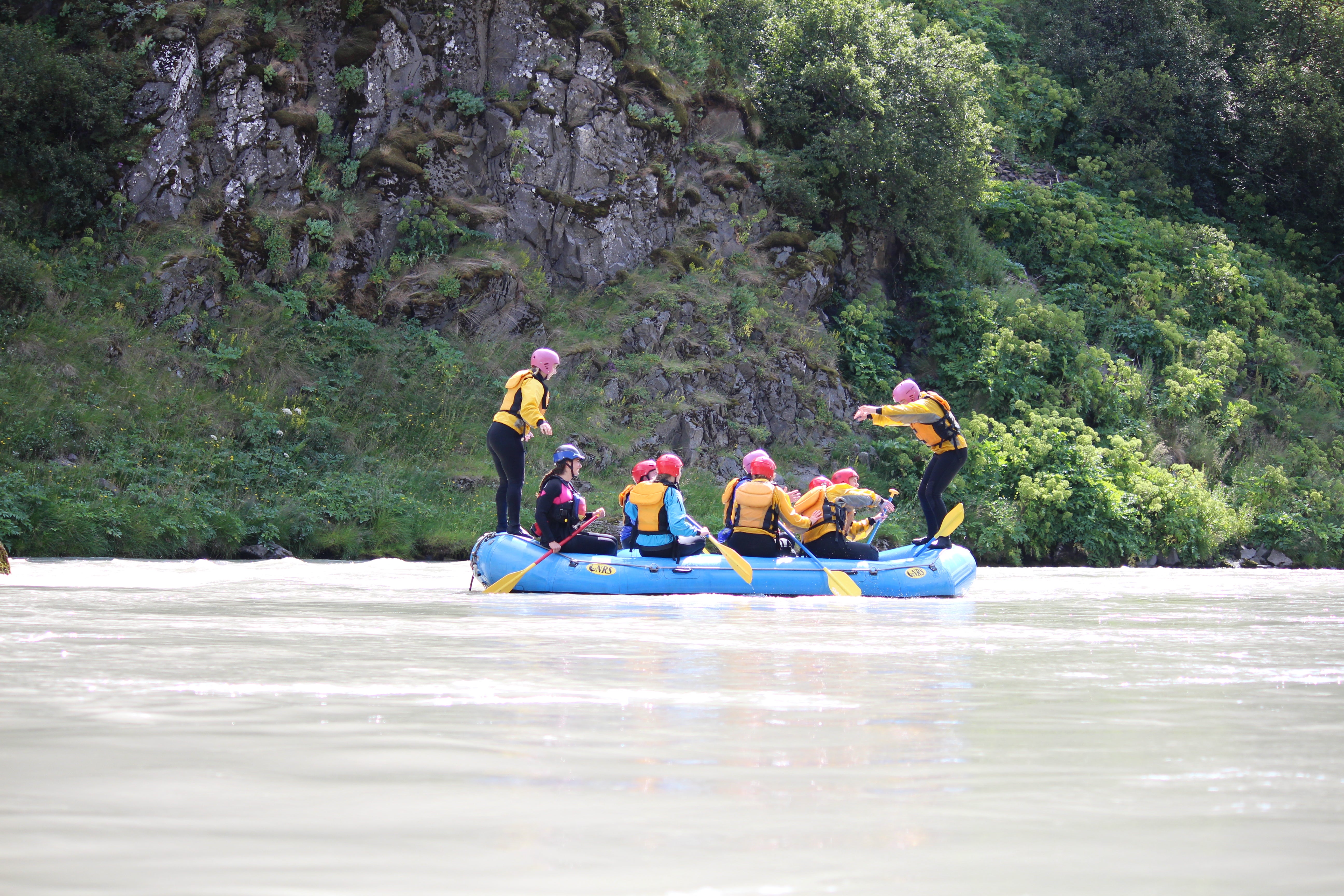 Un groupe de personnes sur un raft dans la rivière Hvita avec une personne debout à chaque extrémité.