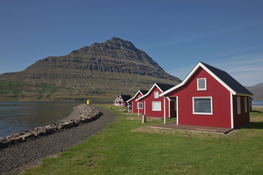 Traditional red painted wooden panel house with mighty Holmatindur mountain in the background in Eskifjordur, East Iceland.