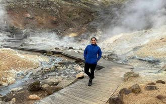 Traveler walking on a boardwalk in Gunnuhver, surrounded by steam and geothermal pools.