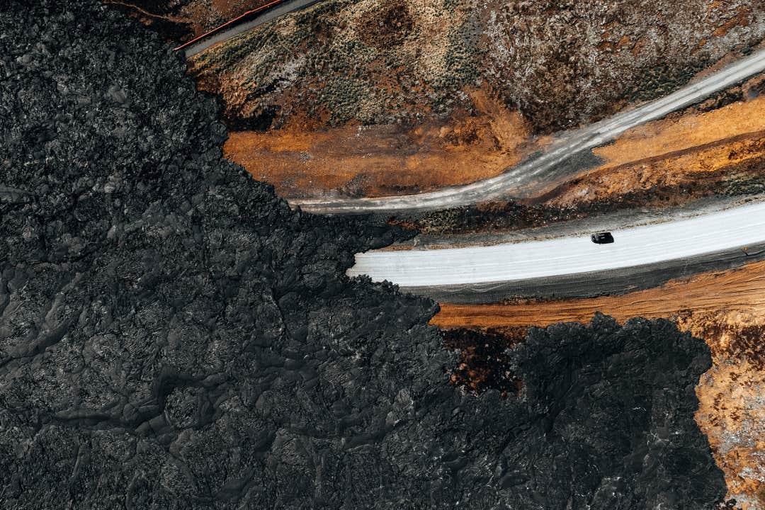 Vue aérienne d’une route près de Grindavik, entourée de champs de lave sombre et de terres orange éclatantes sur la péninsule de Reykjanes, en Islande.