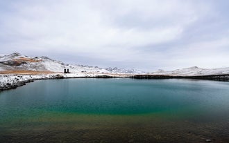 Snow-covered mountains reflected in the vivid green waters of Graenavatn Lake in Iceland’s Reykjanes Peninsula.