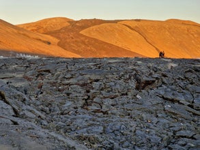 Two people walk along a hardened lava field near the golden slopes of Sundhnukagigar on Iceland’s volcanically active Reykjanes Peninsula.