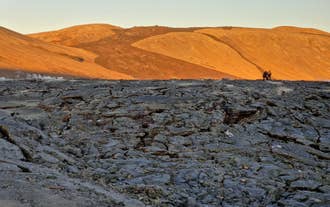 Two people walk along a hardened lava field near the golden slopes of Sundhnukagigar on Iceland’s volcanically active Reykjanes Peninsula.