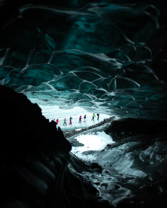 Een groep ijsgrotverkenners loopt over een besneeuwd pad onder een uitgestrekt blauw plafond in het Nationale Park Vatnajokull.