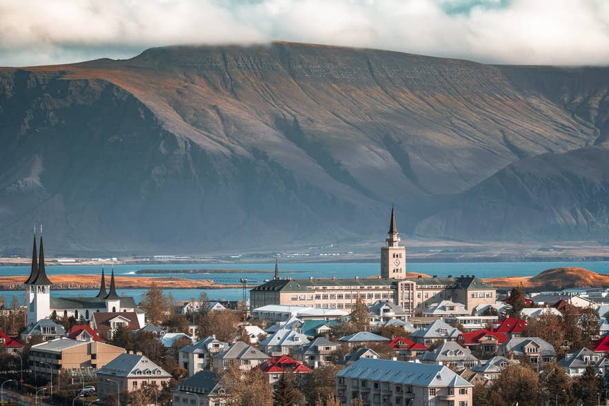 Colorful Reykjavik rooftops and a church spire below Mount Esja in summer, when the coast has no frost nights at all.