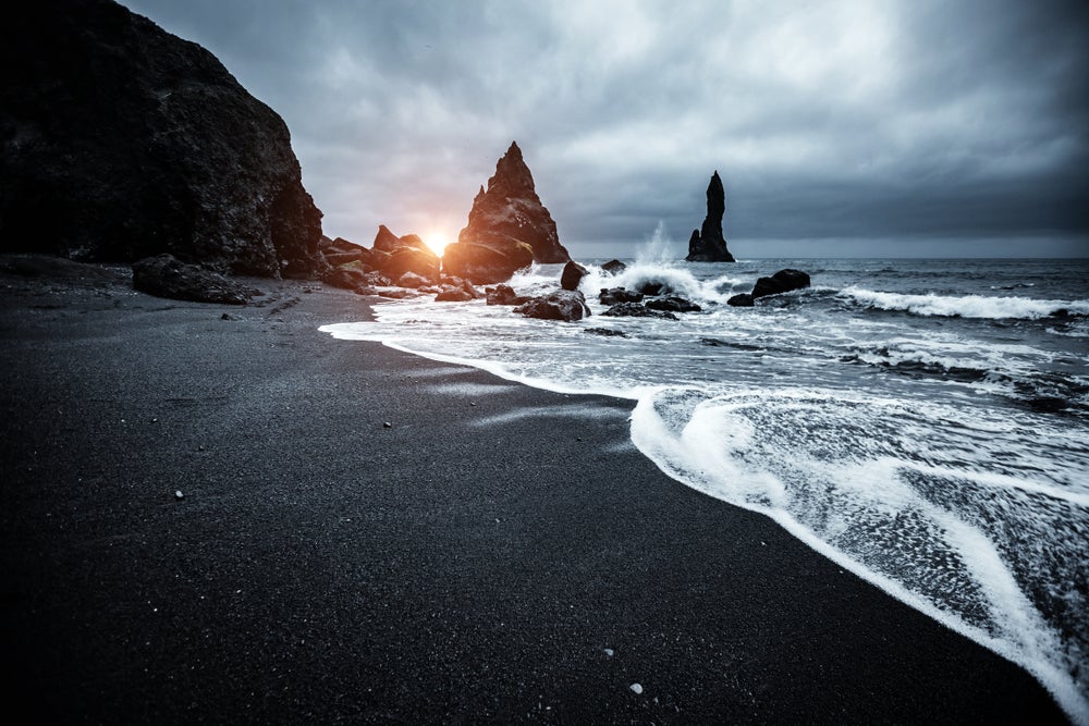 Reynisfjara black sand beach at sunset, with dramatic waves crashing near Reynisdrangar sea stacks on the South Coast of Iceland.