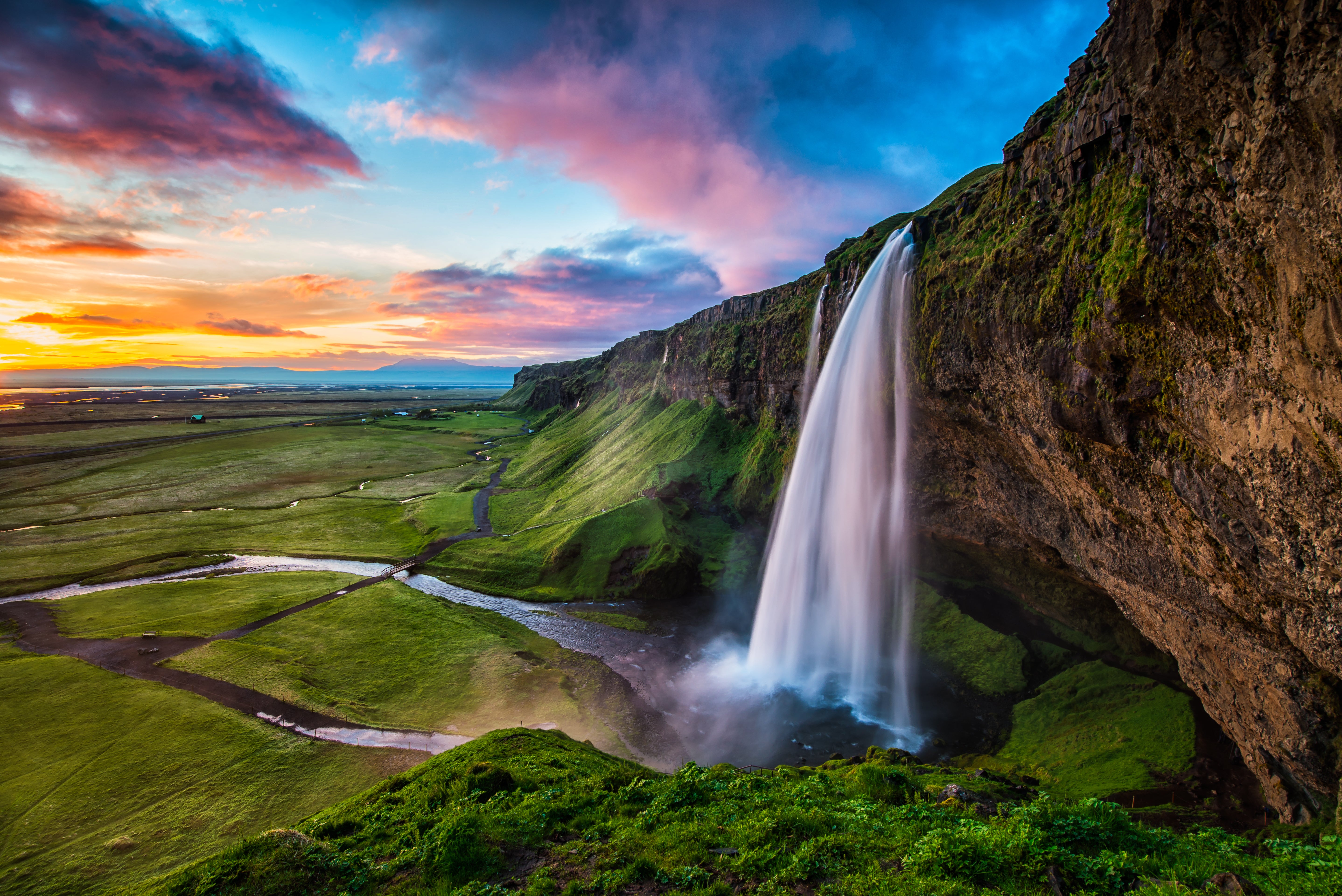 Seljalandsfoss Waterfall cascading down lush cliffs with mist rising at the base.