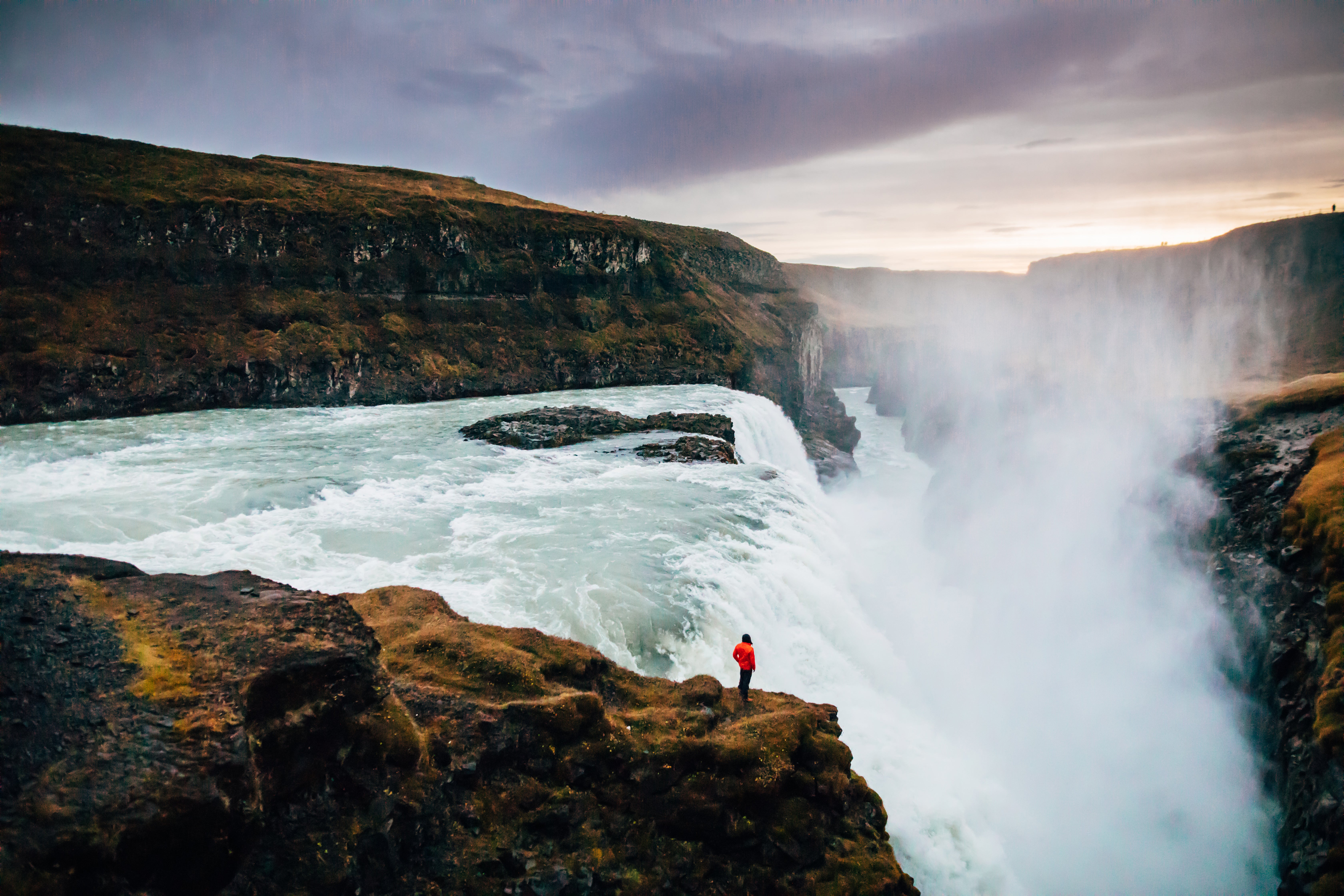 A man in red jacket standing near the edge of Gullfoss Waterfall.