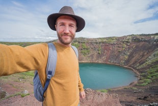 A man in yellow taking a selfie in front of Kerid Crater Lake.