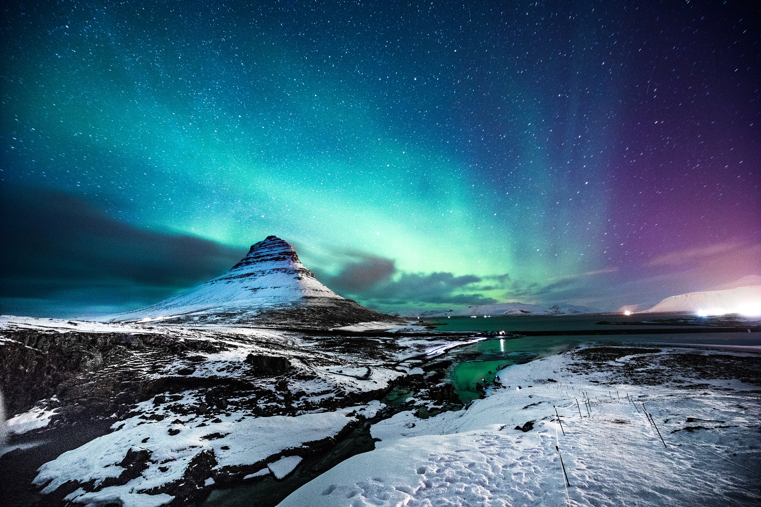 A photo of Kirkjufell Mountain covered with a haze of purple and green northern lights.