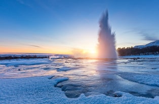 Strokkur Geyser erupts in a powerful steam burst at sunrise, surrounded by icy ground and winter landscape in Iceland’s geothermal area.