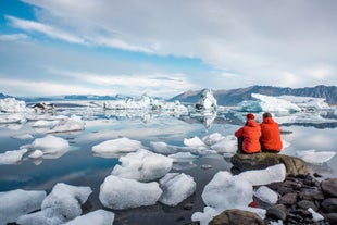 A pair of travelers sits on a rock while admiring the Jokulsarlon Glacier Lagoon.