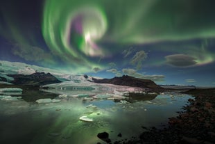 The northern lights dance above Jokulsarlon Glacier Lagoon in Iceland, their vibrant colors mirrored in the glacial meltwater below.