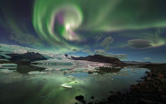 The northern lights dance above Jokulsarlon Glacier Lagoon in Iceland, their vibrant colors mirrored in the glacial meltwater below.