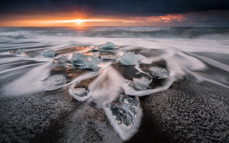 Ice fragments are scattered across Diamond Beach, with the sun setting in the background.