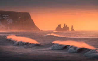 Scena nebbiosa della Costa meridionale dell'Islanda con i faraglioni di Reynisdrangar visibili in lontananza