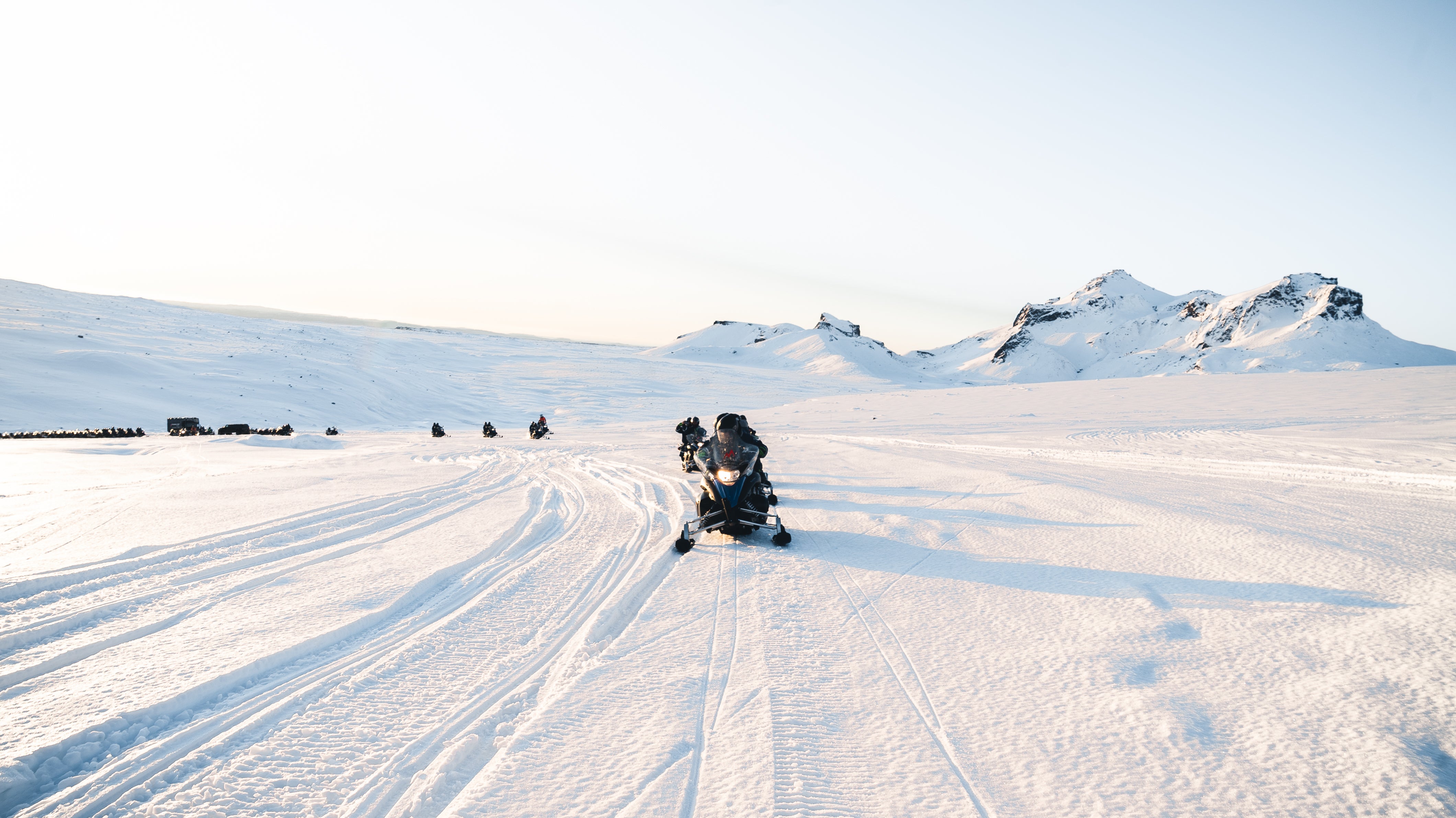 Snöskotrar kör över Islands Langjökull-glaciär under mjukt ljus en klar vinterdag.