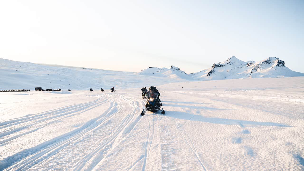 Schneemobile fahren über den Langjökull-Gletscher in Island bei sanftem Licht an einem klaren Wintertag.