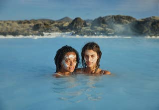 Deux femmes portant des masques à base de boue siliceuse se détendent dans les eaux bleues apaisantes d'un lagon géothermique entouré de roches volcaniques.