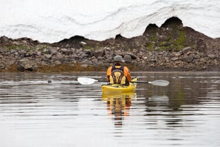 A person wearing a hat in a yellow kayak in the water surrounding the Hornstrandir nature reserve.