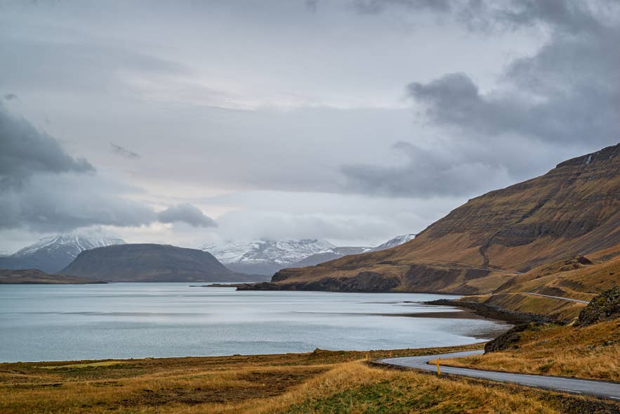 The road curving along Hvalfjordur with snow-capped mountains across the water.