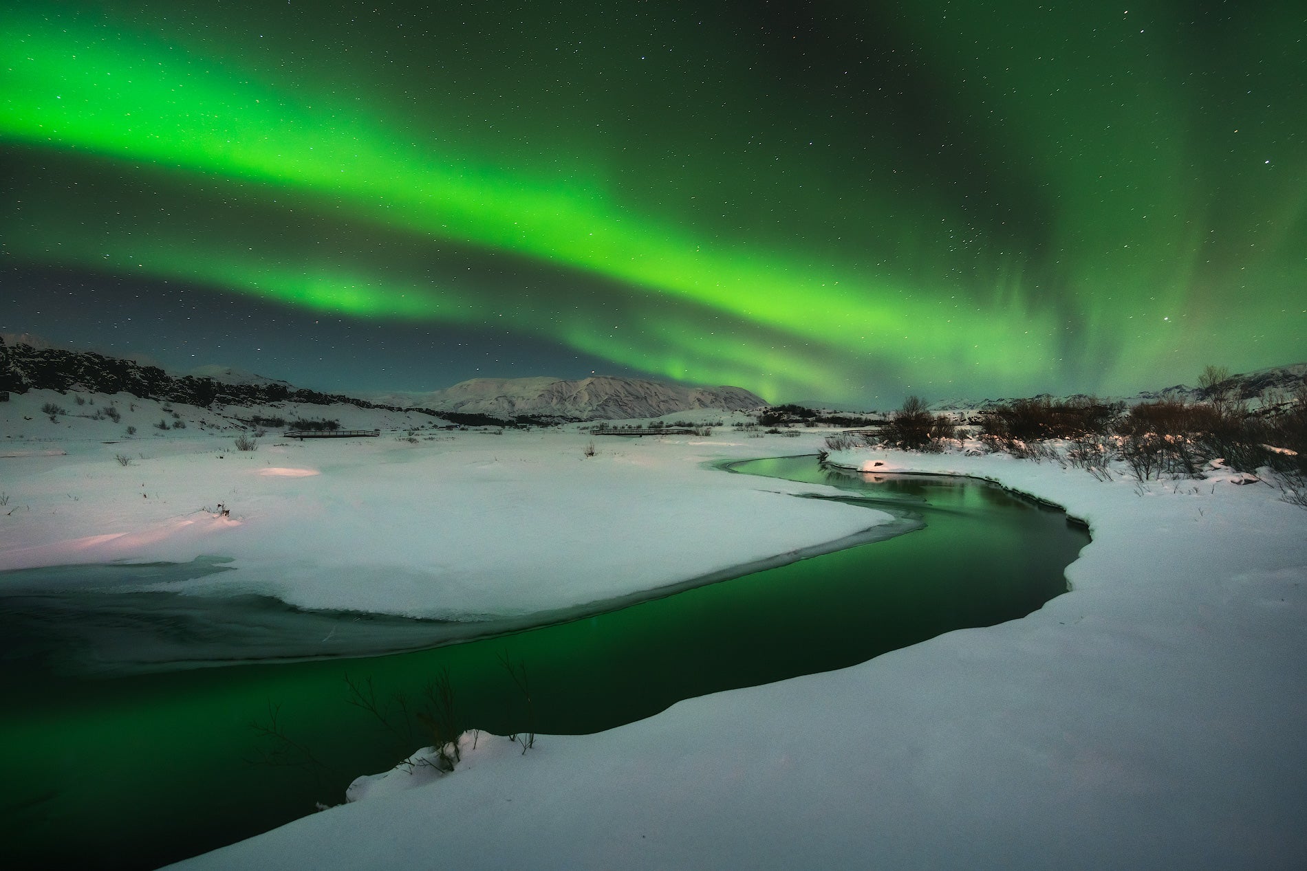 Un'aurora boreale verde illumina il fiume Oxara innevato nel Parco Nazionale di Thingvellir, Islanda.