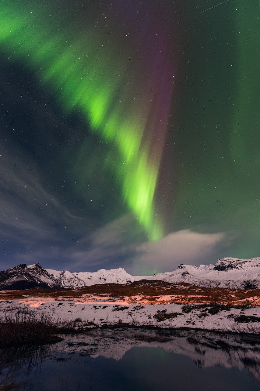 Nordlys lyser over snedækkede bjerge under en klar vinterhimmel i Island.