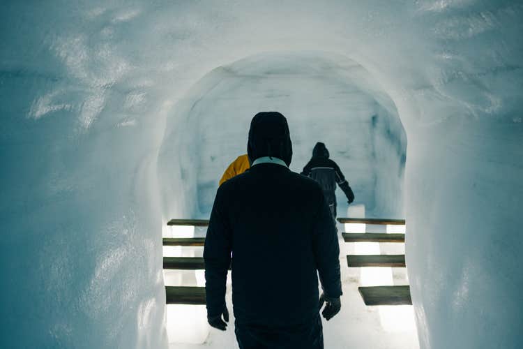 A group of visitors walking through an illuminated ice tunnel with benches carved from ice inside Langjokull Glacier.