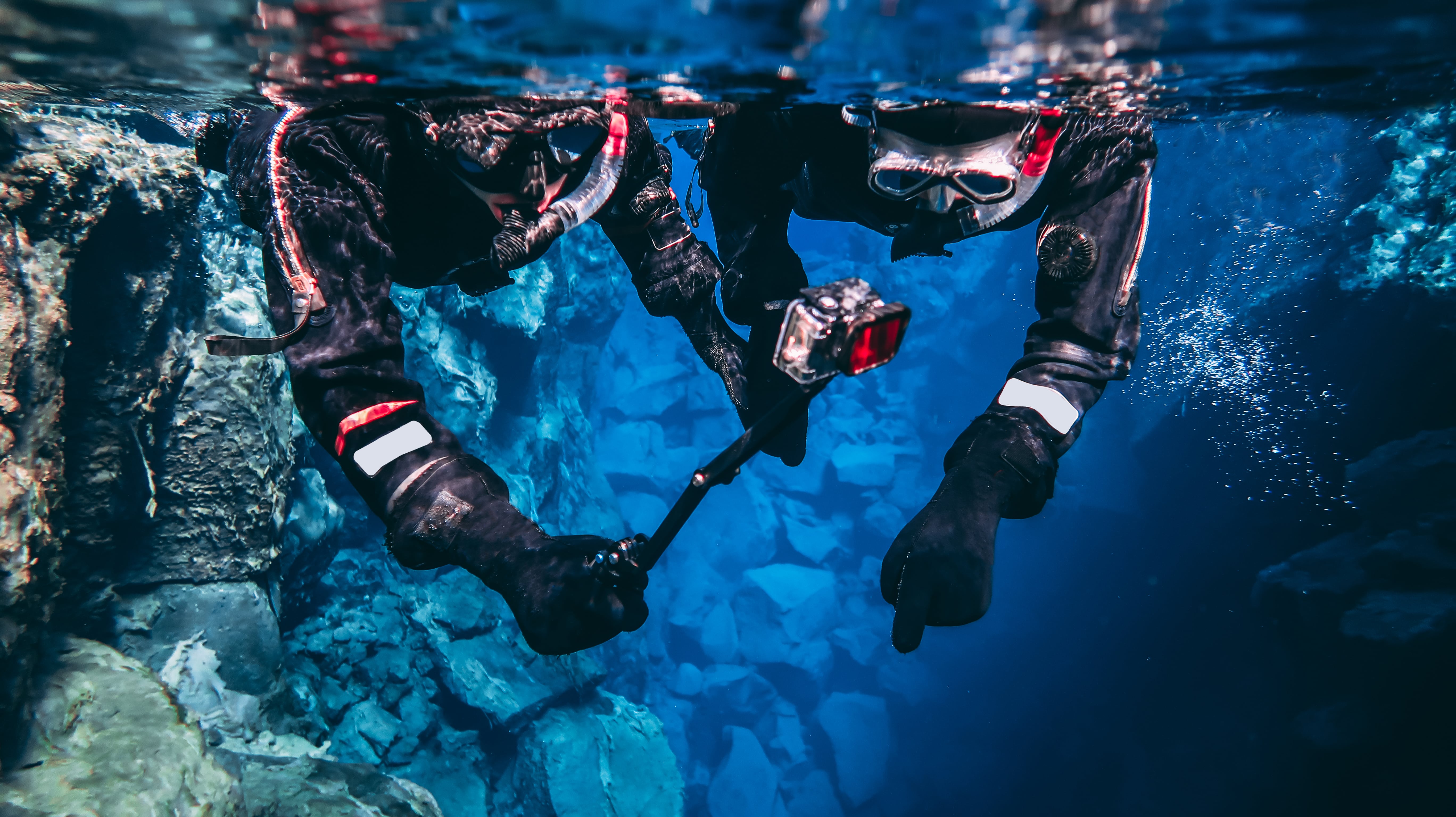 Two snorkelers, equipped with a camera, film underwater in the Silfra Fissure.
