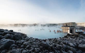Mehrere Menschen entspannen sich im dampfenden geothermischen Becken der Blauen Lagune, umgeben von vulkanischen Felsen.