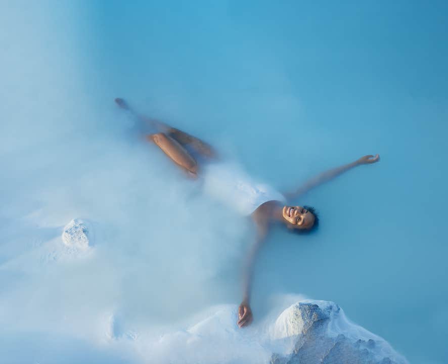 Lachende vrouw drijft ontspannen in het warme, blauwe water van de Blue Lagoon in Grindavík, IJsland.