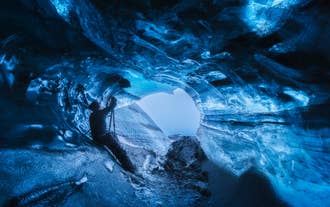 Mann tar bilder i en glødende blå isgrotte i Vatnajökullbreen, Sør-Island.