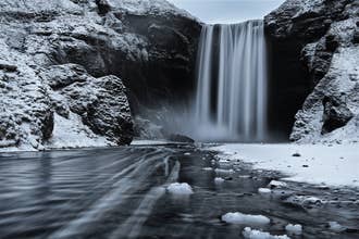Scène hivernale à la cascade de Skogafoss, dans le sud de l'Islande, avec de l'eau glacée et des falaises enneigées.