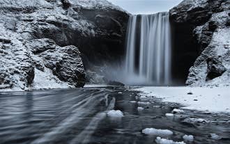 Winterszene am Skogafoss-Wasserfall in Südisland mit eisigem Wasser und verschneiten Klippen.