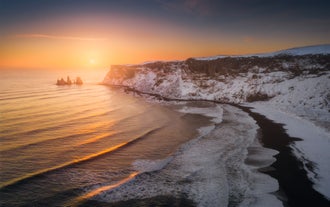 Solnedgång över Reynisfjara svarta sandstrand och snötäckta klippor på södra Island nära Vik.