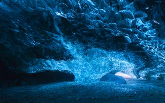 Glowing ice column in Vatnajokull National Park supports shimmering blue cave roof with smooth textures and light filtering in.