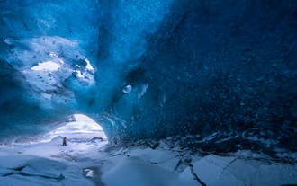 Ein Reisender steht in einer leuchtend blauen Eishöhle am Vatnajökull-Gletscher im Südosten Islands im Winter.